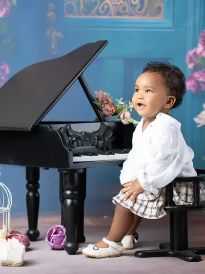 A young musician lost in a happy tune. This toddler portrait at a miniature piano captures a moment of pure, candid joy in a beautifully styled, floral setting.