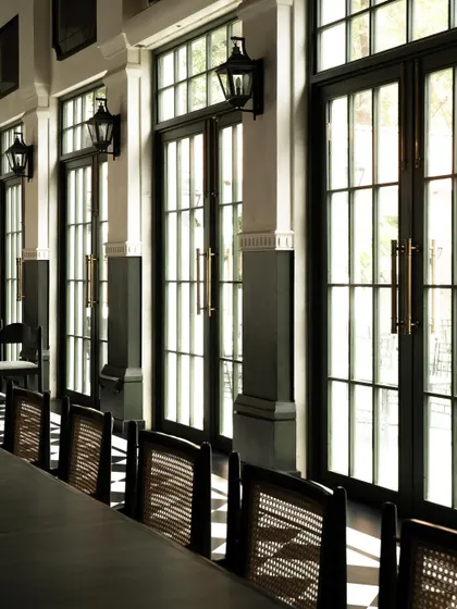 Light filters through the tall gallery windows at Elgin Cafe, casting linear shadows across the space. The woven rattan chairs add a layer of tactile warmth, contrasting with the cool checkerboard floor.
