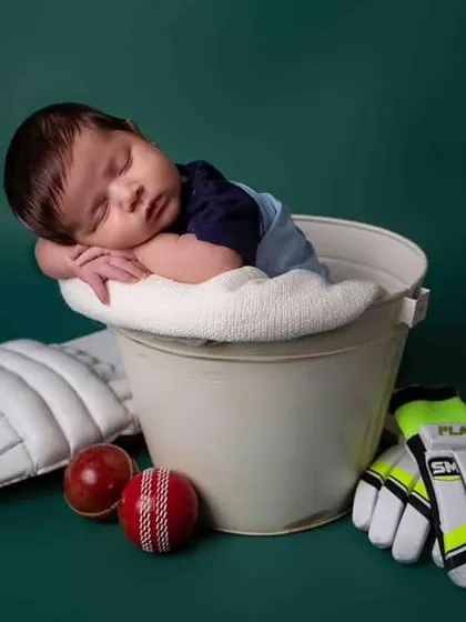 Dreaming of a century! This newborn is posed as a future cricket star, complete with a miniature bat, ball, and pads. A perfect theme for a cricket-loving family.
