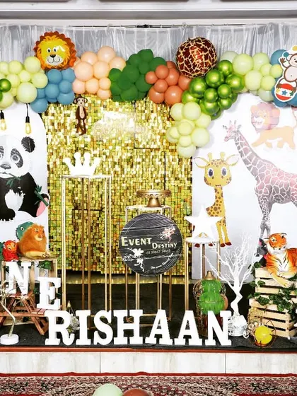 A classic jungle theme for a first birthday party. The decor is filled with friendly animal cutouts, green and brown balloons, and a sparkling gold backdrop.