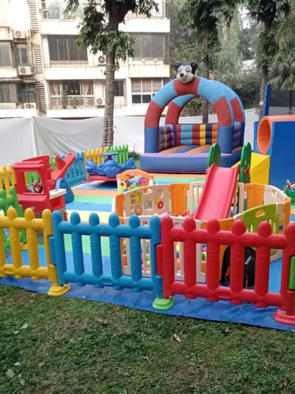 This spacious garden setup includes a large bouncy castle with a slide, a separate ball pit, and plenty of room for kids to run. The entire area is secured with interlocking fences, giving parents complete peace of mind.