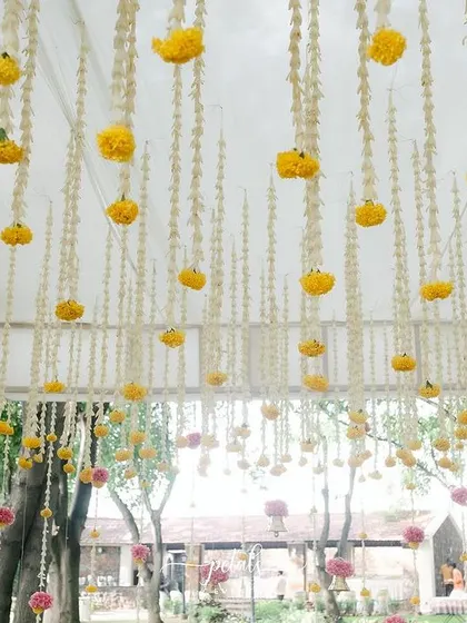 A beautiful ceiling installation for a traditional wedding, featuring hanging strings of yellow marigolds and white tuberoses. This floral canopy transforms the space and adds a festive touch.
