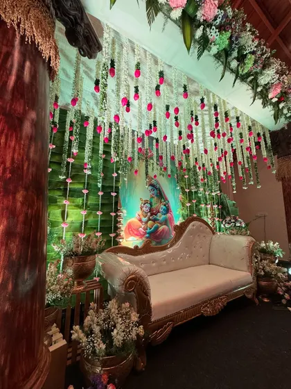 Another angle of the Krishna-themed baby shower decor, showing the depth created by the layered floral hangings and the soft green lighting.
