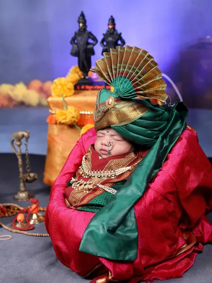 A newborn dressed in a traditional Peshwai-style turban and jewelry for a Maharashtrian cultural shoot. The rich green and red fabrics look stunning against the baby's peaceful sleep.