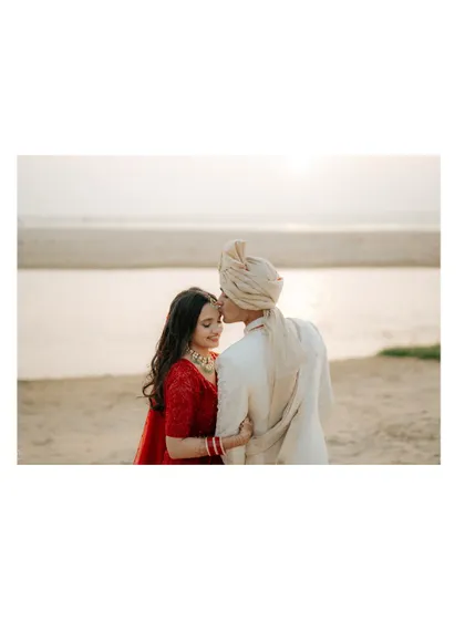 A romantic silhouette of the groom kissing the bride's forehead against the backdrop of the setting sun.