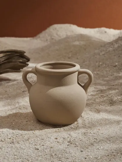A duplicate of image 111, this photo of a small pot in the sand emphasizes its simple, wabi-sabi aesthetic through minimalist styling and natural textures.