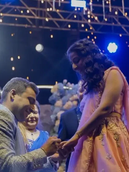 The groom gets down on one knee to put the ring on the bride's finger, a classic and romantic proposal moment.