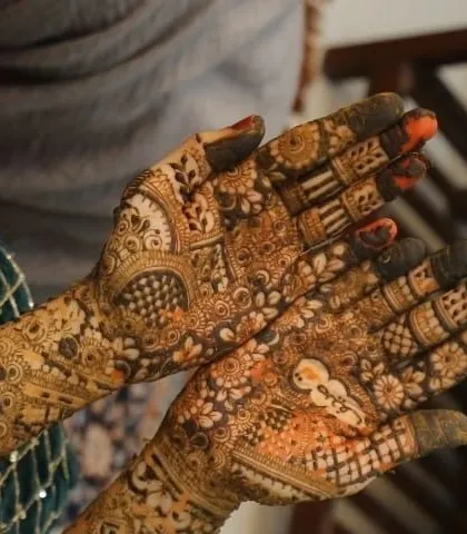A close-up of a bride's palms, showing the semi-dry henna paste. You can see the groom's name hidden in one palm and a floral motif in the other.