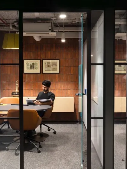 A view into a glass-walled meeting room where a team member is working. The design emphasizes transparency and connectivity.