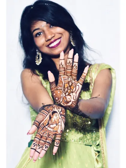 A happy bride displaying her portrait-style mehendi. The design captures the classic bride and groom figures with wonderful detail.