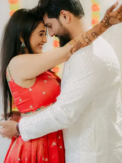 A romantic photo of a couple, with the bride's henna-adorned arm wrapped around her partner.