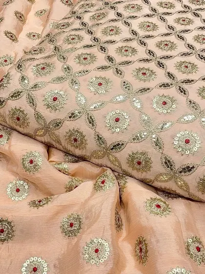This peach-colored Chinon fabric has a warm, inviting tone. The traditional embroidery with silver and red accents makes it a wonderful material for festive salwar kameez or lehengas.