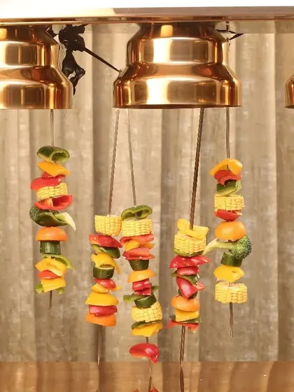 A unique way to serve and keep food warm. These colorful vegetable skewers are hung from a heated lamp stand, creating a visually interesting display and ensuring they are served at the perfect temperature.