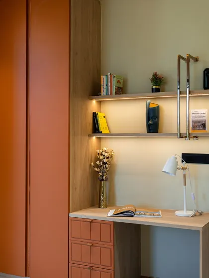 A compact study nook integrated with a wardrobe. The design features an orange accent on the wardrobe door, open shelves with LED lighting, and a sleek desk.