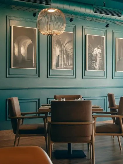 The dining room at Salt and Cravings features deep teal walls with classic molding, creating a sophisticated backdrop for the black-and-white architectural photography. The warm wood tones of the furniture provide a pleasing contrast.