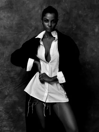 A high-fashion black and white shot with dramatic styling. The contrast between the white shirt and black coat creates a bold, graphic look.