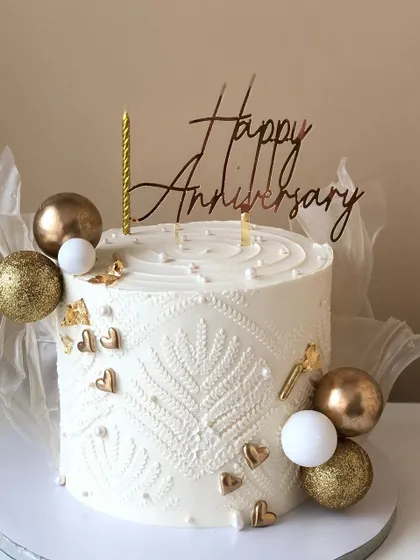 An elegant anniversary cake with a delicate white-on-white stencil pattern and gold and white sphere decorations.