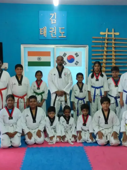 A group of students of all ages and ranks, from yellow belt to red belt, kneels for a photo with their master. This shows the hierarchy and respect that is central to traditional Taekwondo.