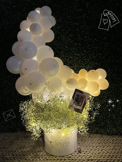 A glowing bouquet with LED fairy lights woven through baby's breath and a cloud of white balloons. This arrangement is magical at night.