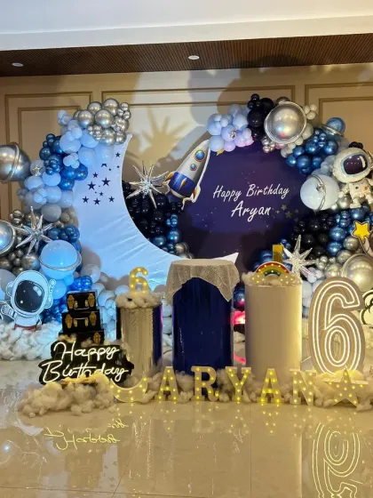 Let's go to the moon! This outer space themed birthday party features a custom crescent moon backdrop, a galaxy of blue and silver balloons, astronaut cutouts, and marquee numbers, creating an out-of-this-world experience for the celebration.