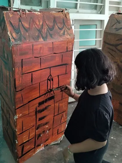 Another student adds the finishing touches to a house for the play. Every child was a participant, contributing their unique skills to the final production.