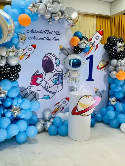 An outer space themed first birthday party. This detailed setup includes a custom backdrop, rocket and astronaut cutouts, and planet-themed props.