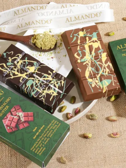 A vibrant and artistic shot of pistachio butter chocolate bars. The green packaging and scattered pistachios are complemented by the creative chocolate drizzle, making for a visually exciting product photo.