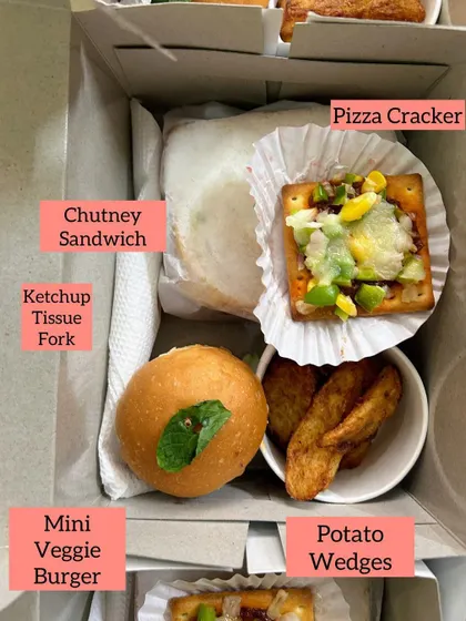 A closer look at one of my custom snack boxes. This one contains a Mini Veggie Burger, a classic Chutney Sandwich, crispy Potato Wedges, and a cheesy Pizza Cracker, along with ketchup and a napkin.