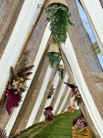 A creative walkway tunnel made from jute and white fabric panels. The path is lined with floral arrangements, creating a rustic and charming entrance.