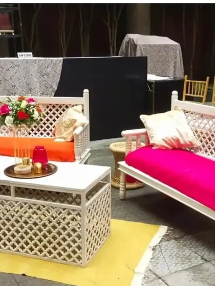 A vibrant and comfortable lounge area created for a Mehendi party, using white lattice-work sofas with bright pink and orange cushions.