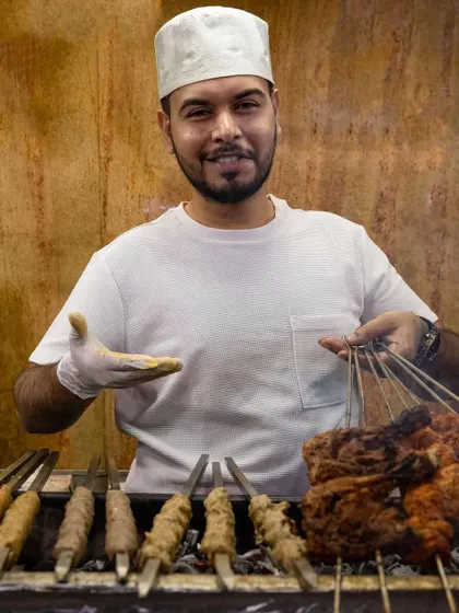 One of our proud chefs presenting freshly grilled Chicken Tikka and Seekh Kebabs. We serve every dish with a smile, knowing we are sharing our family's heritage.