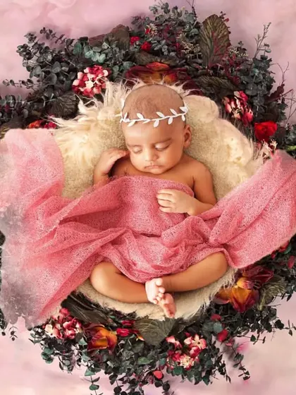 A newborn wrapped in a pink cloth, resting in a nest decorated with red and green foliage.