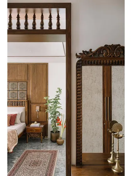A closer look at the parents' bedroom, where Chettinad motifs are carried through in the carved mirror frame and architrave. The wardrobe, with its fabric-laminate shutters, stands beside traditional brass lamps, creating a cohesive and culturally rich space.