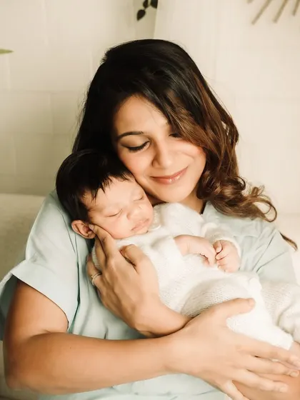 A mother's serene smile as she cuddles her sleeping newborn in the warm light of the studio.