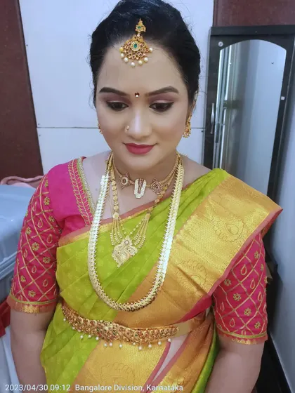 A radiant look for a baby shower ceremony. The makeup features a soft, glowing base with subtle eye definition and a natural lip color, allowing the beautiful green and pink Kanjeevaram saree to shine.