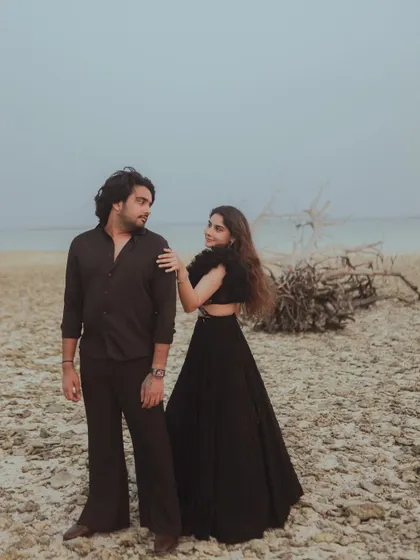 A stylish portrait of the couple on a rocky beach, with their all-black outfits making a bold statement against the muted tones of the sky and sea.