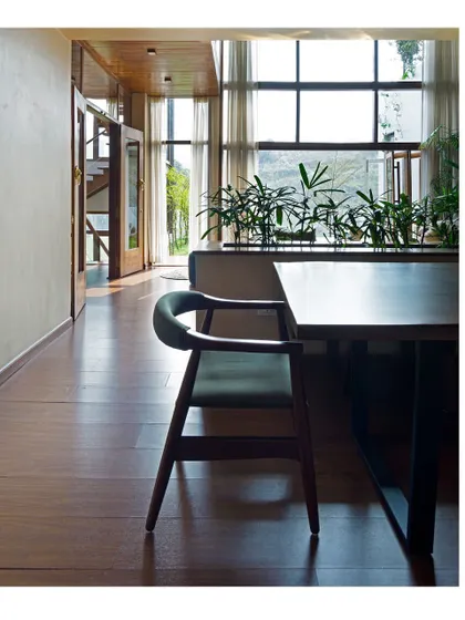 Simplicity and natural materials define the dining space. The clean lines of the wooden furniture and flooring are complemented by the natural light and greenery, creating a calm and inviting atmosphere for family gatherings.