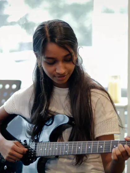A student guitarist focused on her performance. Our recitals showcase the diverse talents of our musicians.