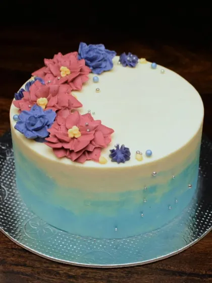 A simple and elegant cake with a blue ombre base. The top is decorated with a crescent of hand-piped buttercream flowers in shades of dusty rose and blue.