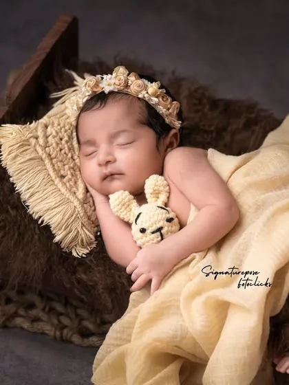 A sleeping newborn girl cuddling a tiny bunny, resting peacefully in a rustic wooden bed.