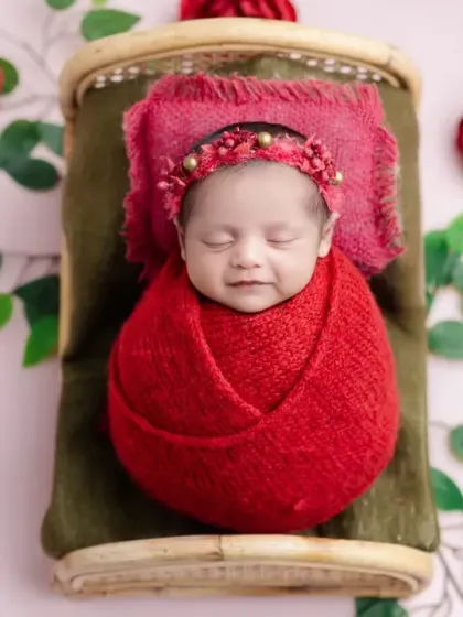 A smiling newborn in our red rose setup, looking cozy and content.