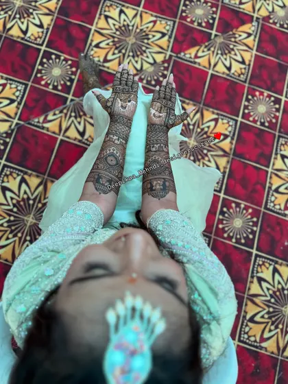A creative top-down view of the bride and her mehndi. This artistic shot showcases the beauty of the henna against the colorful floor, with the bride's face gently blurred.
