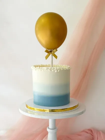 A simple and elegant cake with a blue ombre buttercream finish. It's topped with a single, statement gold balloon for a modern, minimalist celebration.