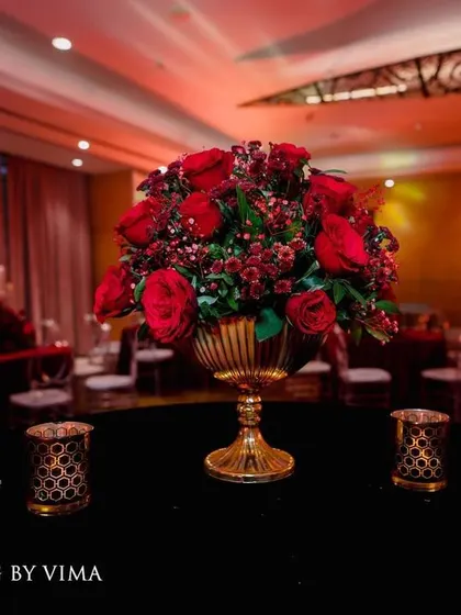 A luxurious centerpiece featuring a bouquet of deep red roses in a golden vase. This classic and elegant detail was part of a glamorous red-themed reception.