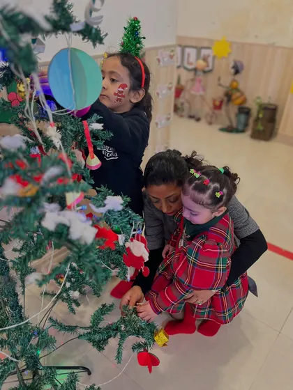 An instructor helps a toddler decorate the Christmas tree, a wonderful collaborative activity that brings everyone into the holiday spirit.