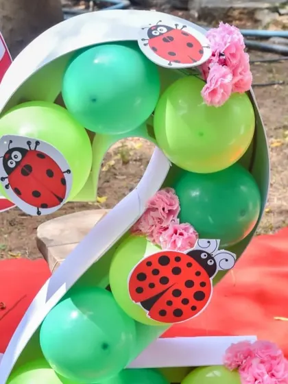 A custom-made number "2" filled with green balloons and decorated with ladybugs for a second birthday party. This personalized decor element is perfect for photos.