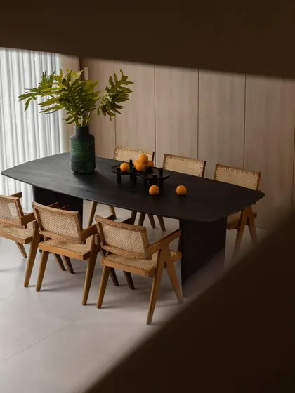 A top-down view of a dark wood dining table surrounded by Pierre Jeanneret-style cane chairs. This setup is a perfect example of timeless mid-century modern design.