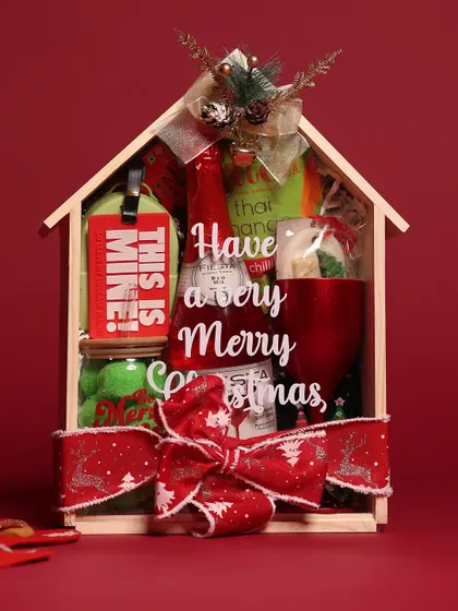 A studio shot of the wooden house Christmas hamper, showcasing the "Have a very Merry Christmas" message and the curated items inside.