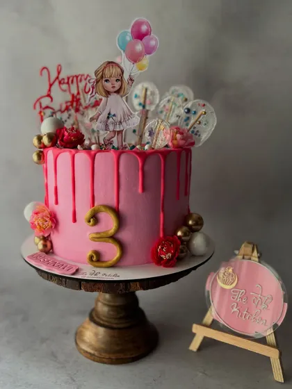This pink drip cake is perfect for a little girl's birthday, featuring a cute character topper, lollipops, and balloons.