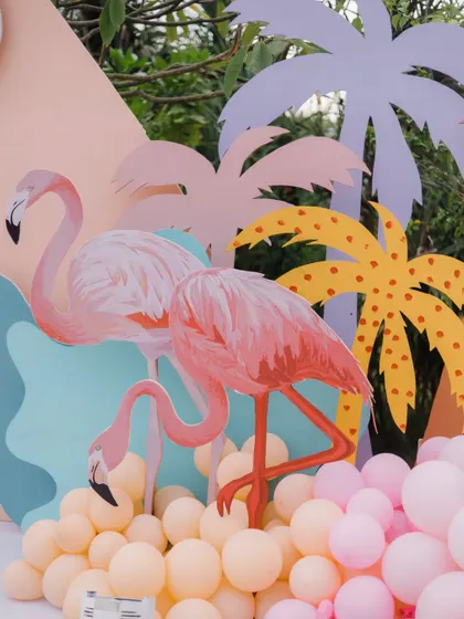 A vibrant photo booth with hand-painted flamingos and palm trees, surrounded by pastel balloons for a fun pool party.